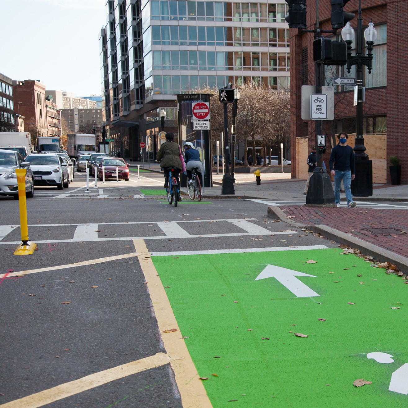 Two bicyclists ride in a contraflow bike lane separated from opposing traffic with by a parking lane and flexposts