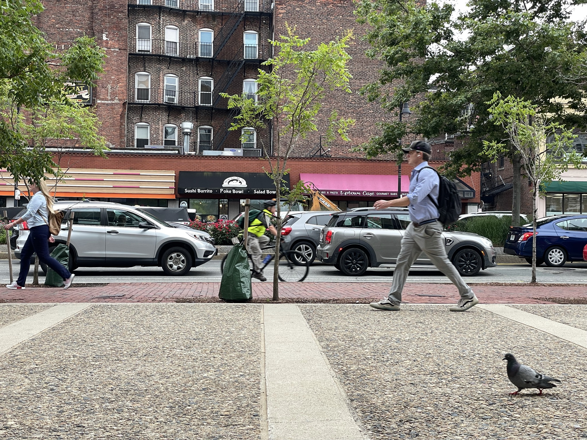 People walking on a sidewalk on Cambridge Street near Staniford Street; a cyclist is riding in the road.