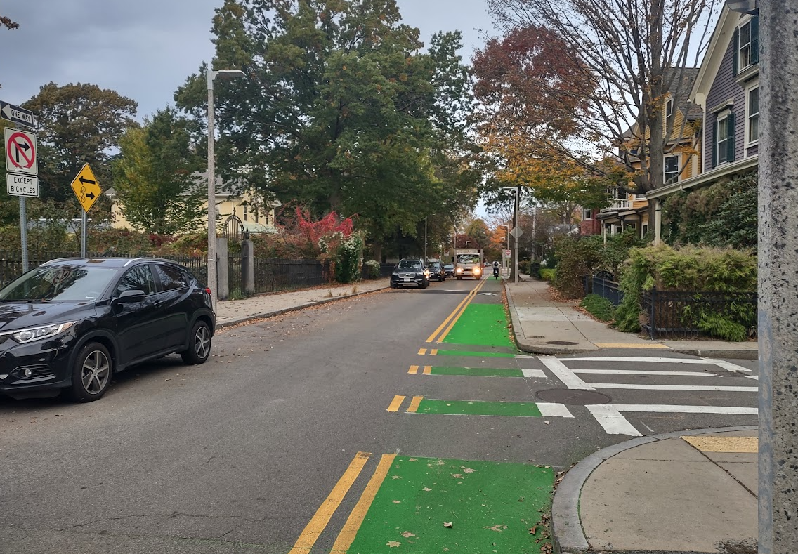 A photo showing a contra flow bike lane on Eliot Street. A bicyclist is riding in the lane.