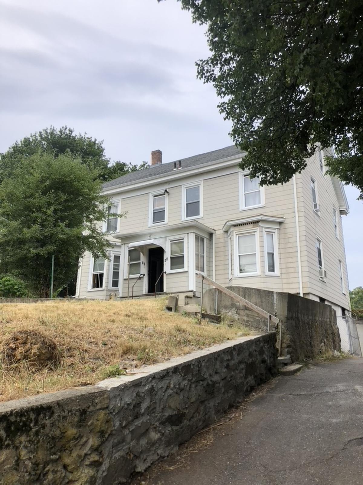 A two-family house sitting on a hill with a brick wall and driveway
