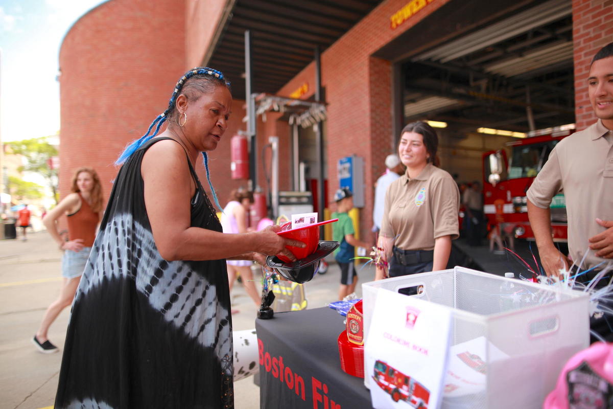 Open Streets Boston, woman with blue braids holding two fire fighter helmets in front of the fire house