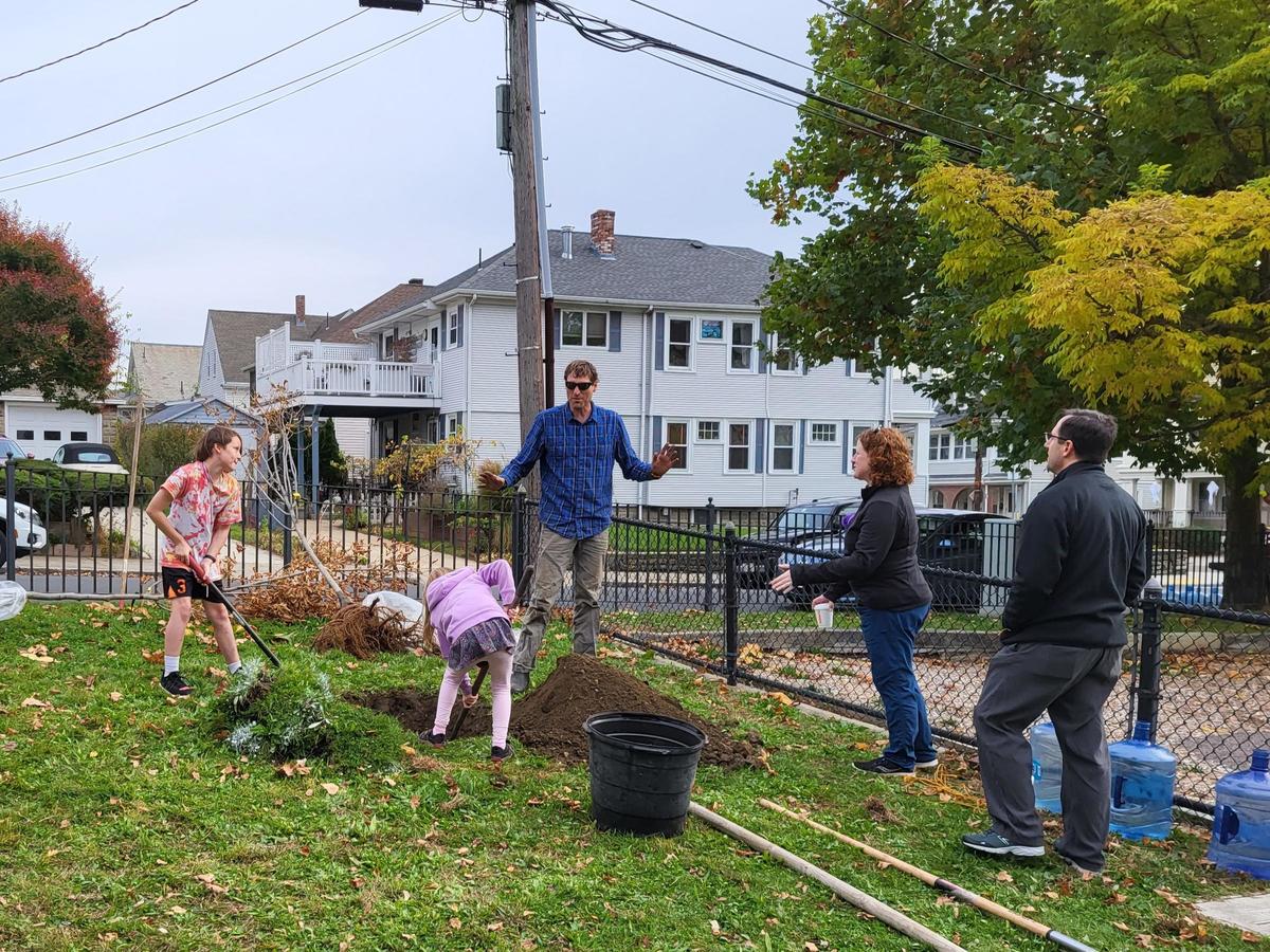 Two children dig a hole in Hobart Park as an adult speaks to two other volunteers. The trees to be planted are in the background.