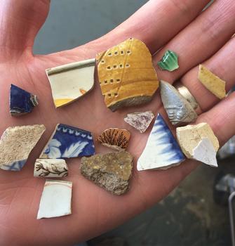 A close up of a hand holding an assortment of ceramic sherds ranging from the 17th to 19th centuries in date.